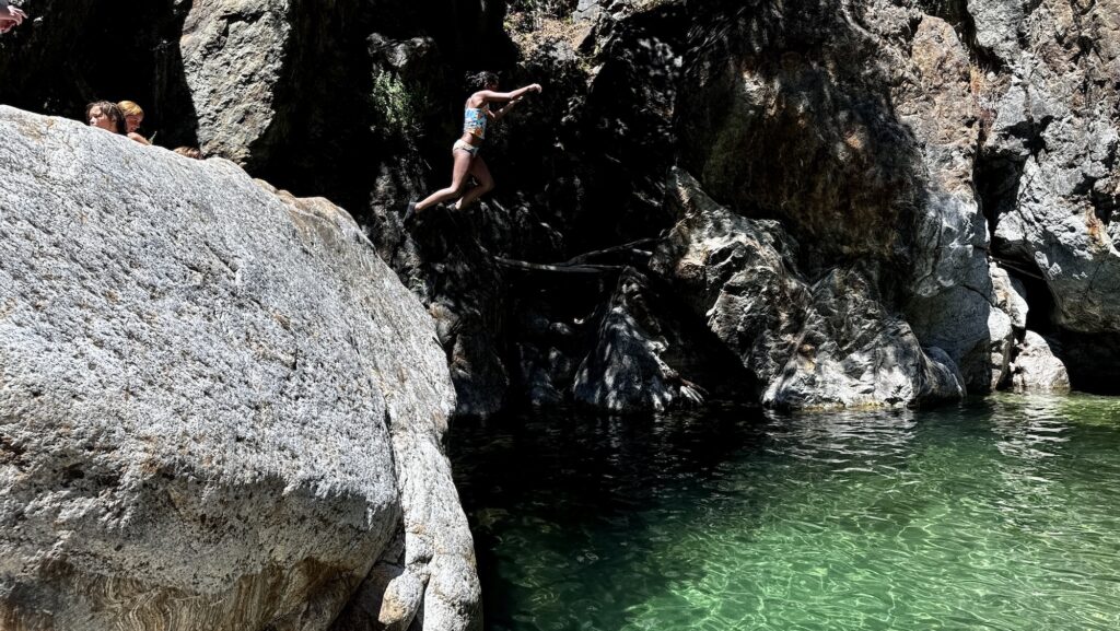 teen jumping from a large rock into a swimming hole on a summer day in Big Sur